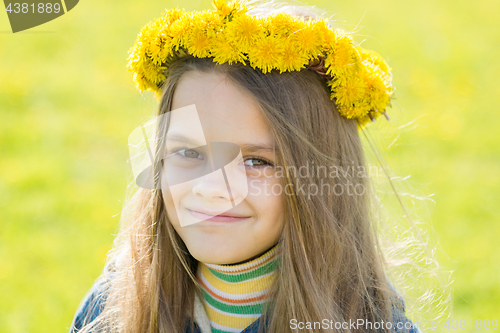 Image of Portrait of a happy eight-year-old girl with a wreath of dandelions on her head, against the background of a spring clearing