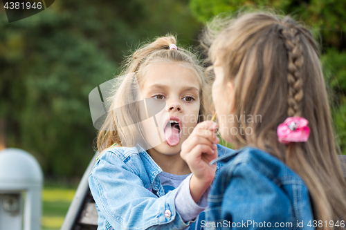 Image of One girl treats another girl with her lollipop