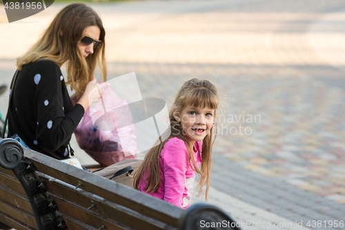 Image of Six-year-old girl and mother sat on a bench for a walk, the girl joyfully looked at the frame