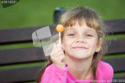 Image of Portrait of a six-year-old cheerful girl who holds a lollipop in her hand and looks pleased at the frame