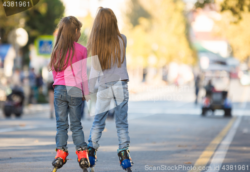 Image of Two girls girlfriends rollerblading on the mall, rear view