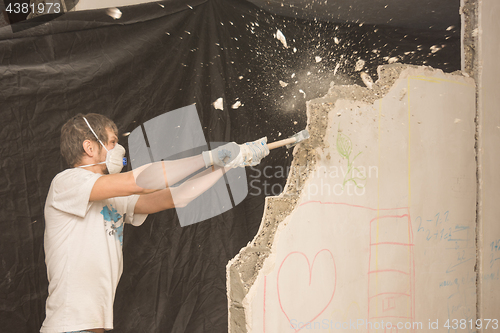 Image of A young man breaks a partition in the apartment with a hammer