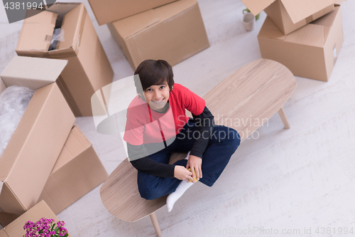 Image of boy sitting on the table with cardboard boxes around him top vie