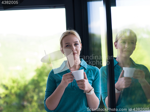 Image of young woman drinking morning coffee by the window