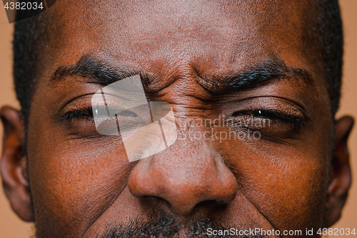 Image of The squint of Afro American stylish man at brown studio wall