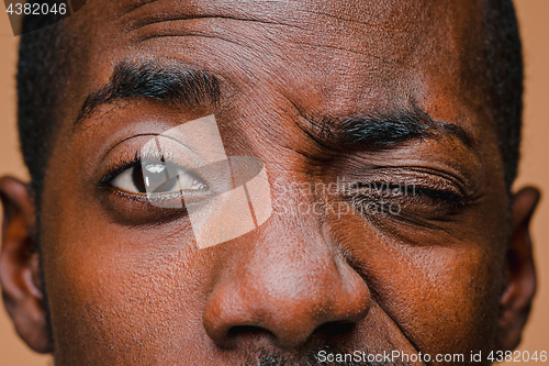 Image of The squint of Afro American stylish man at brown studio wall