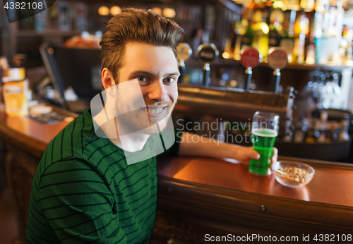 Image of man drinking green beer at bar or pub