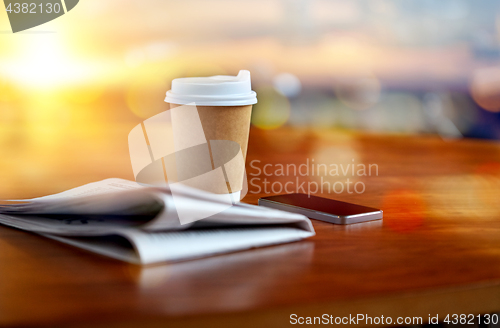 Image of coffee cup, smartphone and newspaper on table