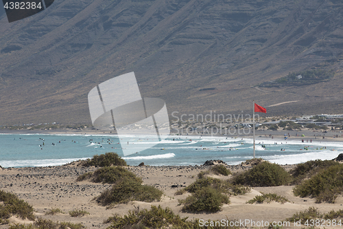 Image of The red flag weighs in the wind at Surfers Beach Famara on Lanza