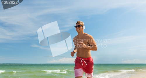 Image of happy man with headphones running along beach