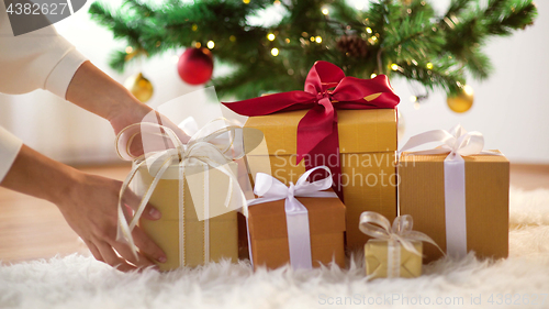 Image of hands putting gift boxes under christmas tree