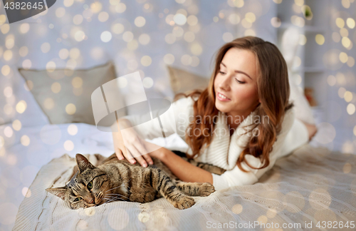 Image of happy young woman with cat lying in bed at home