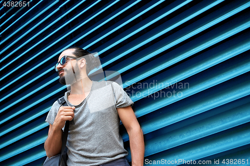 Image of man in sunglasses with bag standing at street wall