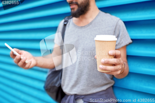 Image of man with coffee cup and smartphone over wall
