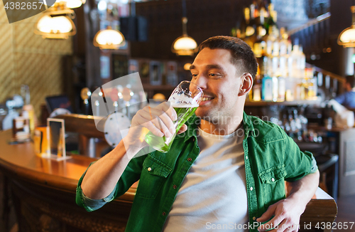 Image of man drinking green beer at bar or pub