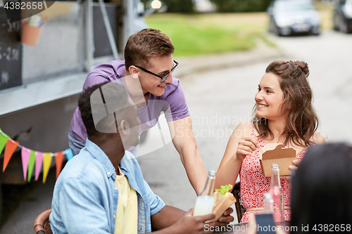 Image of happy friends with drinks eating at food truck