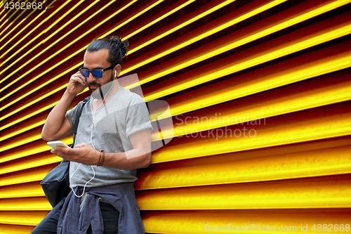 Image of man with earphones and smartphone over wall