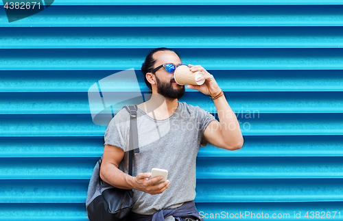 Image of man with smartphone drinking coffee over wall