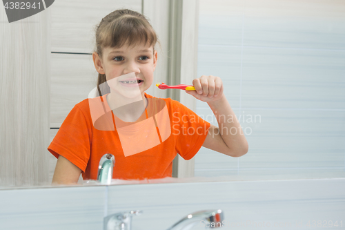 Image of Seven-year-old girl looks at herself in the mirror before brushing her teeth
