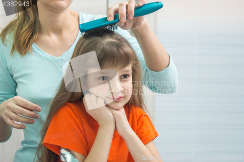 Image of A beautiful daughter looks cute in the mirror while Mom combs her hair