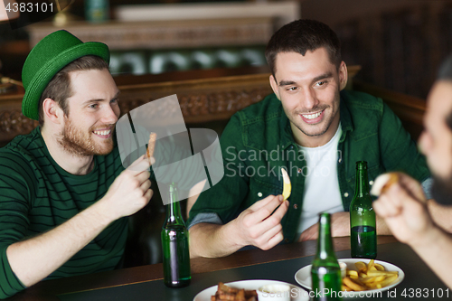 Image of male friends drinking green beer and eating at pub