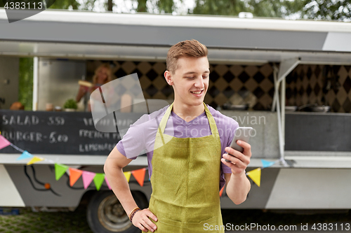 Image of salesman in apron with smartphone at food truck