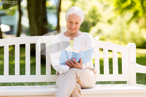 Image of happy senior woman reading book at summer park