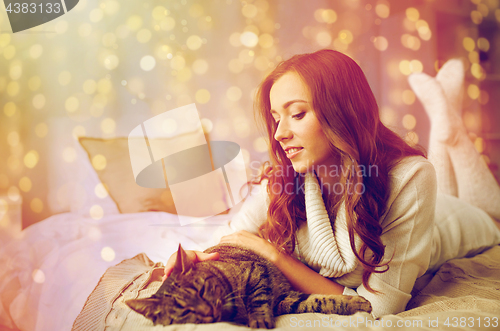 Image of happy young woman with cat lying in bed at home