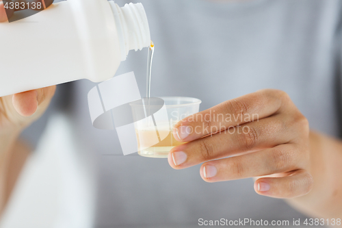 Image of woman pouring syrup from bottle to medicine cup