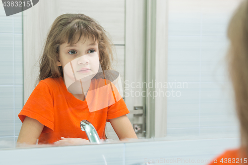 Image of Seven-year-old girl looks at herself in the mirror, in the bathroom