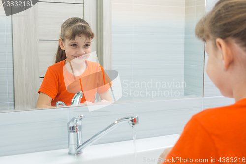 Image of Seven-year-old girl washing her face looks at herself in the mirror