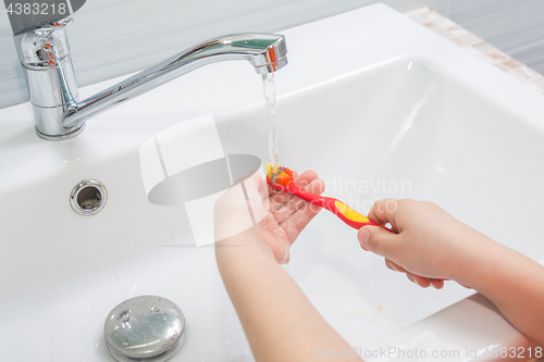 Image of The child rinses the toothbrush under running water
