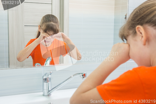 Image of Seven-year-old girl rubs her eyes trying to wake up, washing in the morning in the bathtub