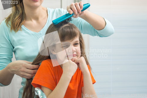 Image of The daughter gnaws looking in the mirror while Mom combs her hair