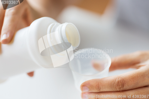 Image of woman pouring syrup from bottle to medicine cup