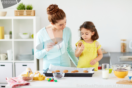 Image of happy mother and daughter eating cookies at home