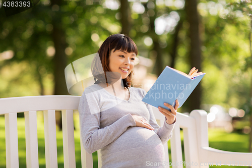 Image of happy pregnant asian woman reading book at park