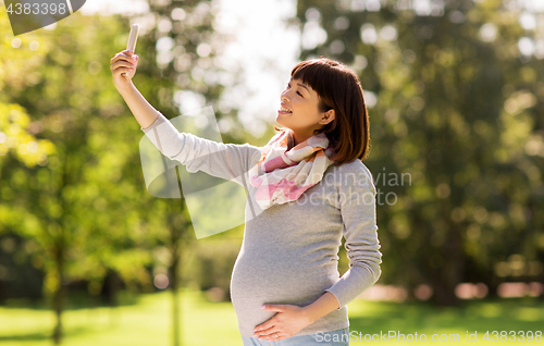 Image of happy pregnant asian woman taking selfie at park