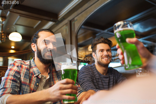 Image of male friends drinking green beer at bar or pub