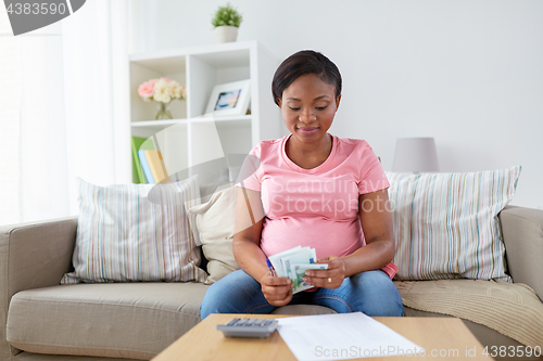 Image of happy pregnant woman counting money at home