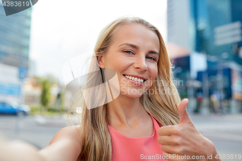 Image of happy young woman taking selfie on city street