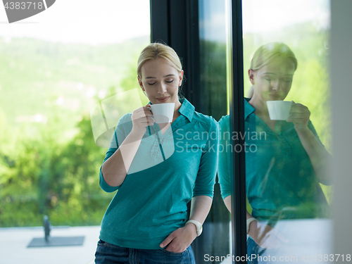 Image of young woman drinking morning coffee by the window