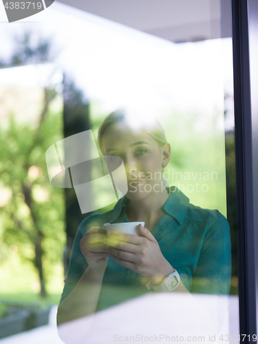 Image of young woman drinking morning coffee by the window