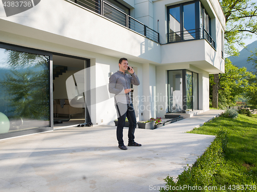 Image of man using mobile phone in front of his luxury home villa