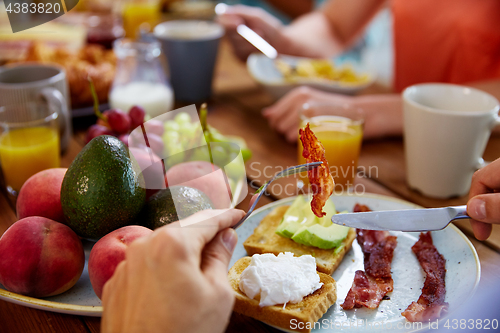 Image of hands with bacon on fork at table full of food