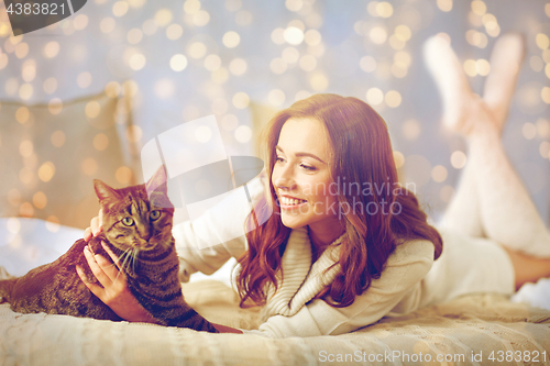 Image of happy young woman with cat lying in bed at home