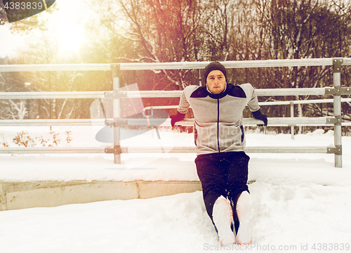 Image of sports man doing triceps dips at fence in winter