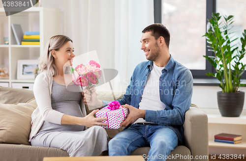 Image of man giving flowers to pregnant woman at home