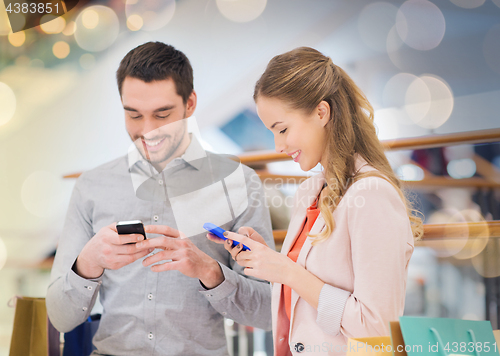 Image of couple with smartphones and shopping bags in mall