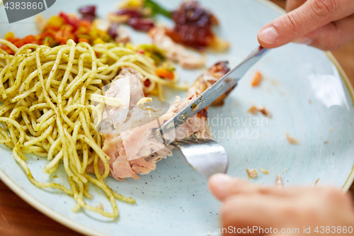 Image of close up of hands eating chicken meat with pasta